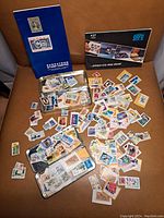 Large assortment of loose postage stamps spread out, with blue Saskatoon Stamp Centre album and several metal tins visible.