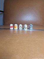 Front view of five collectible ceramic thimbles lined up next to a ruler for scale.