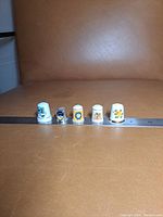 Front view showing five thimbles including four porcelain and one metal with colorful printed designs and patterns.