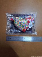 Photo shows colorful McDonald's toy sealed in original plastic packaging, placed on a surface next to a ruler for size reference approximately 7 cm long.