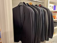 Photo showing six men's sport jackets hung on a rack in various dark colors