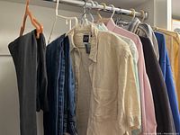 Photo shows multiple men's clothing items hung on hangers including shirts and trousers in various colors and patterns.