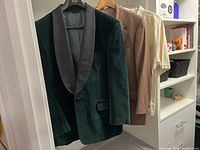 Green velvet men’s dinner tuxedo jacket, brown checkered blazer, and beige casual shirt hanging in a closet on hangers
