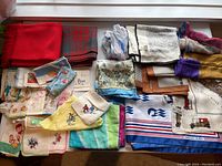 Collection of vintage hankies and scarves laid out showing variety of colors and prints including embroidery and wool plaid