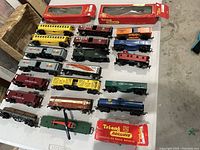 Wide view showing 21 assorted Tri-ang O O gauge railway cars in various colors and styles on white table including several in original boxes.