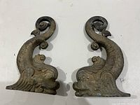 Front view of the pair of cast brass Victorian dolphin andirons showing detailed fish and dolphin head design.
