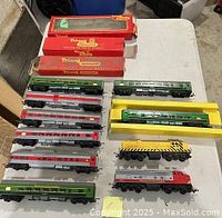 Two sets of Tri-ang OO gauge electric trains laid out on a table, showing red, grey, and green passenger cars and original boxes
