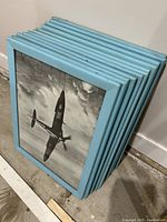Stack of 8 framed WWII Battle of Britain aircraft prints with sky blue frames, showing minor frame wear.
