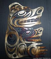 Close-up photo of bronze-colored metal artwork of a bear with cub in Salish art style on a black background.