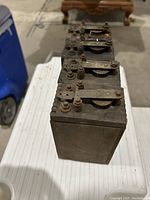 Four rectangular wooden ignition coils arranged vertically, viewed from the front terminals with metal mountings and connection bolts visible on top.