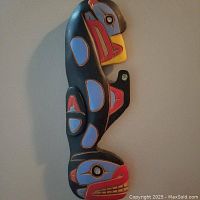 Front view of the carved wooden figure painted in black, red, blue, and yellow with traditional Salish patterns.