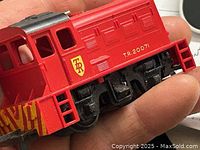 Red model locomotive held in hand, showing front and side with T.R. 20071 markings and yellow striped detailing.