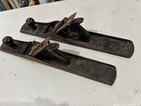 Two Stanley No. 7 Bailey wood planes side by side showing overall length and profile with dark handle knobs and metal bodies.