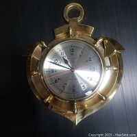 Overall view of brass nautical anchor shaped clock with round metallic face on black background