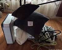 Photo of stacked decor cushions, knit throw blanket, and a large pile of assorted hangers on floor.