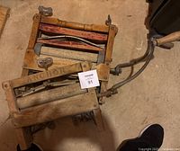 Photo showing both antique wooden hand crank clothes wringers stacked together on floor, one labelled 'ANCHOR' on the frame.