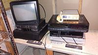 14-inch Citizen TV atop black VHS players in stack with visible remote controls on shelf.