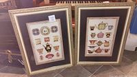 Two gold framed wall art prints side by side on floor showing designs of teapots and porcelain plates.