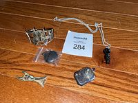 Overview photo showing the cuff bracelet, fish shaped charm, two silver lockets, and a necklace with a carved pendant on a silver chain.