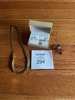 Full view of jewelry set on wooden floor with white box containing ring and earrings, two rings outside the box, and two necklaces laid out.