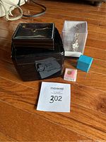 Photo of all items included in the lot on wooden floor: Hudson watch in plastic box, black travel jewelry box, tie chain in box, small pendant charm in a small box, ring in blue box.