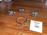 Four silver-tone cuff bracelets laid out on wooden floor, including three with large oval tiger's eye stones and one twisted snake design bracelet.