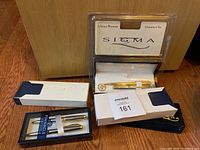 Pen and pencil sets from Pinnacle in black cases, Sigma ballpoint pen in gold in plastic display box with warranty card, and Bill Blass pen and pencil in black velvet box.