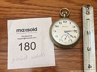 Front view of antique Helvetia pocket watch beside ruler showing size about 2.5 inches