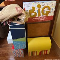 Stack of assorted card boxes and envelopes arranged on the floor, including striped, floral and solid color boxes with a burlap bag.