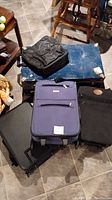 Five pieces of luggage including three medium suitcases, a computer bag, and a blue trunk grouped on floor under chairs