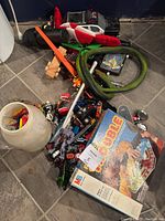 Overview photo showing assorted toys scattered on the floor including a Trouble board game, assorted figurines, a green snake toy, and various small toy parts.
