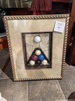 Frontal photo showing the shadow box frame with pool balls arranged in a triangular rack. The frame has a gold decorative edge and the balls are positioned on a textured cracked background.