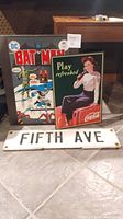 Fifth Ave street sign, Coca Cola wall plaque, and Batman canvas displayed together on floor
