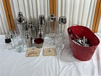 Full display of the lot with stainless steel shakers, glasses, red bucket with bar tools, ice bucket, coasters.