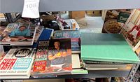 Photo showing a stack of various cookbooks including Rocco DiSpirito, Mad Hungry, and a green hardcover cookbook.