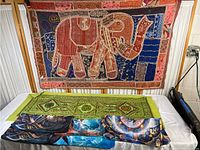 Display of the elephant fabric wall hanging mounted vertically above a table with four colorful decorative pillowcases laid out flat below it.
