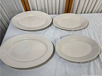 Four white Homer Laughlin china platters arranged on a white cloth surface, showing variations in size.