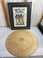 Full view of framed Egyptian fabric print and round wooden manifestation board together on table
