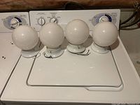 Four ceiling lights shown side by side on top of a white washing machine. Each has a round white glass globe and a white base with wires extending from it.