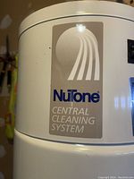 Close-up of NuTone logo and central cleaning system label on the white central vacuum unit.