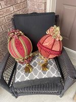 Two decorative balls placed on an outdoor wicker chair with cushion, showing detailed ornamental features.