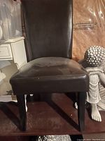 Front view of one faux leather parson chair showing padded seat and backrest with black wooden legs; slight wear visible on seat surface