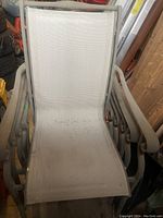 Close up front view of one patio chair showing beige metal frame with mesh fabric seat and back, some staining visible on fabric.