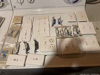 Overview photo showing an assortment of toggle switches, wall plates, and electrical outlets arranged on a surface.