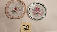 Top view showing the two porcelain plates, one round with green and pink floral design and gold trim, the other square-shaped with pink lattice border and floral center with gold trim.