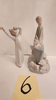 Front view of the two porcelain figurines, lady with pigs and girl yawning on a white background with lot number 6