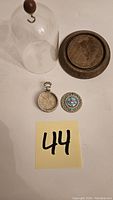 Photo of glass dome, wooden base, and pocket watch case arranged on white surface with lot number 44 visible