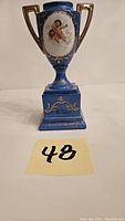 Front view of the blue and gold Austrian porcelain trophy with cherub artwork and gold detailing on the base and handles.