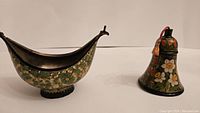 Front view of a boat-shaped hand painted wooden bowl with floral detailing and a bell with hand painted floral decoration.