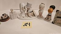 Porcelain figurines arranged in a row including a bride and groom, children, and gift box figurines.